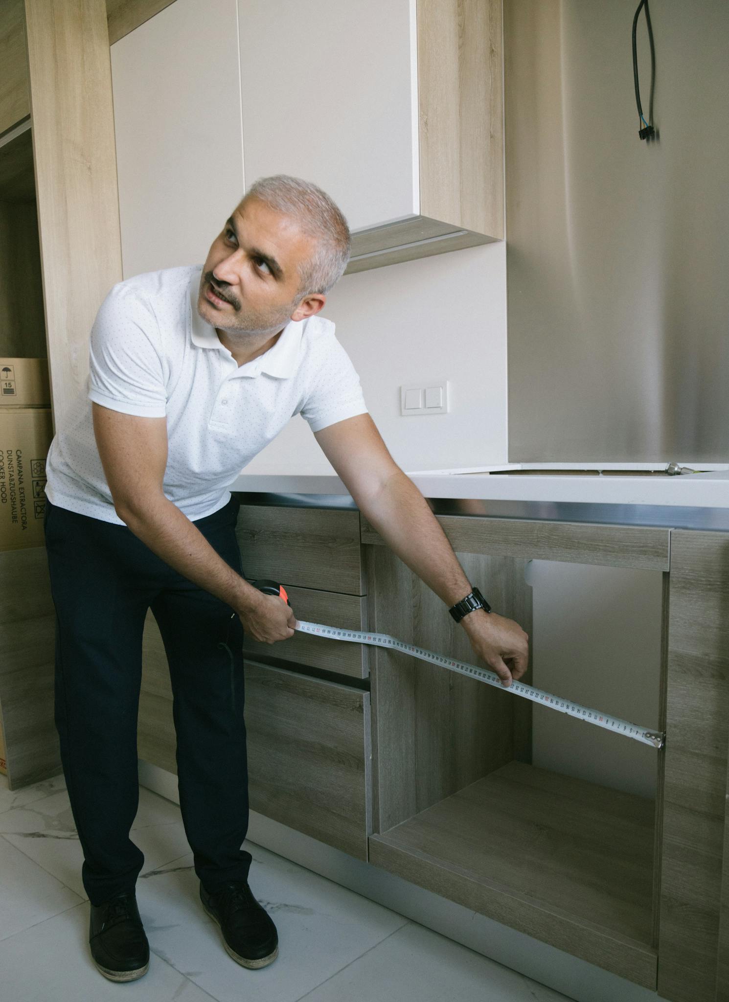 A man using a measuring tape to measure kitchen cabinets in a modern Istanbul apartment.