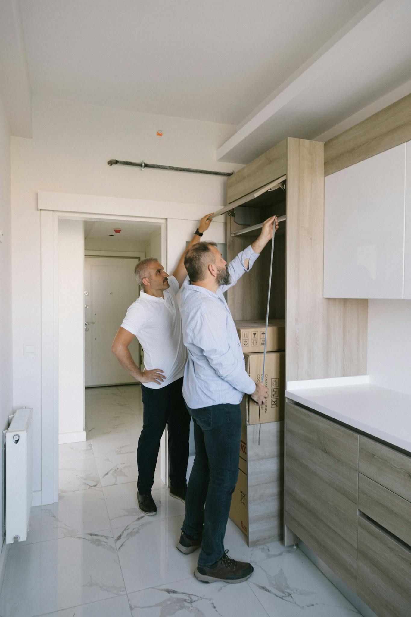 Two men measuring a modern kitchen cabinet for a renovation project in an apartment.